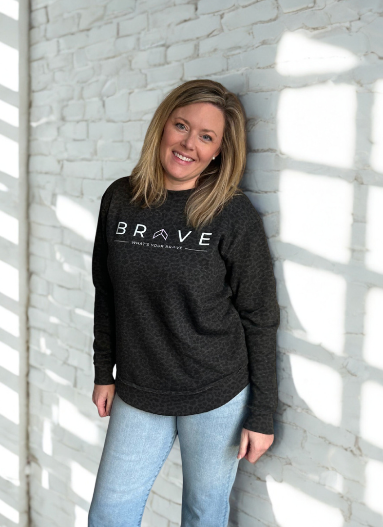 Mom wearing a black sweatshirt with 'BRAVE' text, standing against a white brick wall.
